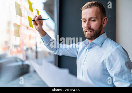 Geschäftsmann schreiben auf Haftnotizen an der Glasscheibe Stockfoto