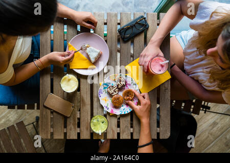 Blick von oben auf die drei jungen Frauen an den hölzernen Tisch sitzen mit Smoothies und Kekse Stockfoto