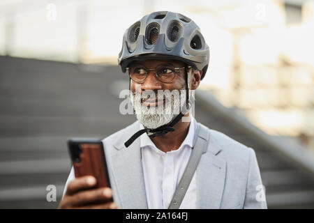 Portrait von lächelnden reife Geschäftsmann mit Smartphone das Tragen von Helm und Brille Stockfoto