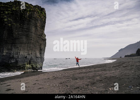 Frau auf Lava Beach im Südosten von Island, laufen und springen vor Freude Stockfoto