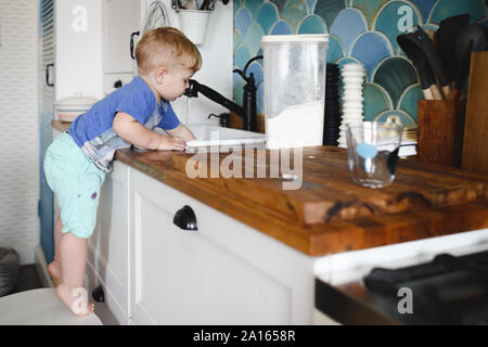 Kleiner Junge stand auf Zehenspitzen auf Stuhl in der Küche Geschirr spülen Stockfoto