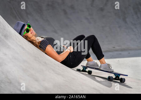 Junge Frau mit Skateboard liegend im Skatepark Stockfoto