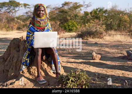 Traditionelle Muhila Frau, Turnschuhe tragen, Neakers arbeitet sie an ihrem Laptop, Kehamba, Chibia, Angola Stockfoto