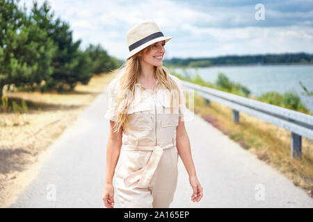 Lächelnde Frau gehen auf die ländliche Straße am See Stockfoto