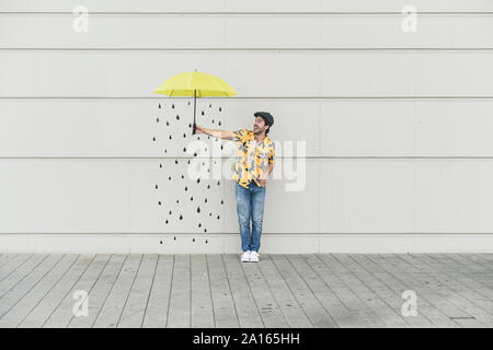 Digital composite junger Mann hält einen Schirm an der Wand mit Regentropfen Stockfoto