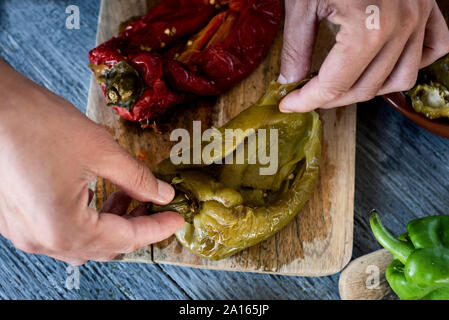 Hohe Betrachtungswinkel eines Mannes peeling Einige gegrilltes Gemüse wie Paprika, Paprika, Tomaten und Zwiebel, escalivada vorzubereiten, ein Gericht typische Stockfoto