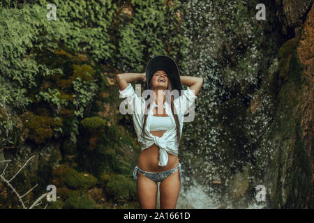 Glückliche junge Frau mit Hut stehend in der Nähe von einem Wasserfall Stockfoto