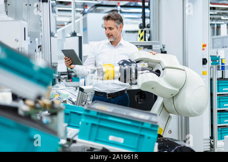 Geschäftsmann mit Tablette montageroboter in einer Fabrik Stockfoto