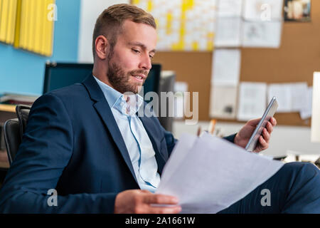 Geschäftsmann mit Papieren und Tablet am Schreibtisch im Büro Stockfoto