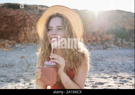 Glückliche junge Frau mit einem Smoothie am Strand Stockfoto