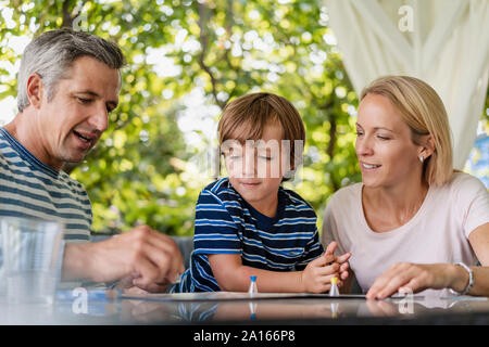 Glückliche Eltern und Sohn spielen ein Brettspiel auf der Terrasse Stockfoto