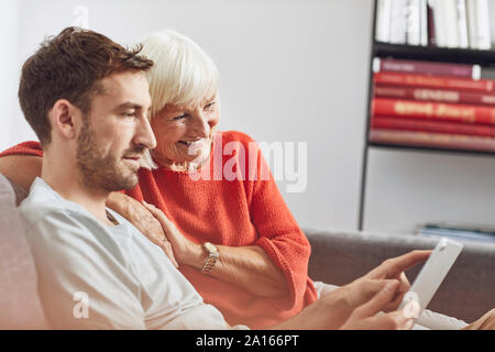 Der Enkel sitzt auf der Couch, mit digitalen Tablet mit seiner Großmutter Stockfoto