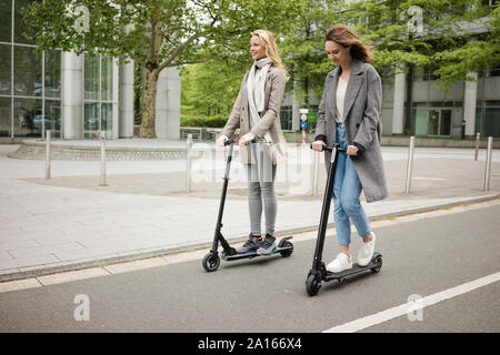 Junge Frauen reiten Elektroroller auf der Straße Stockfoto