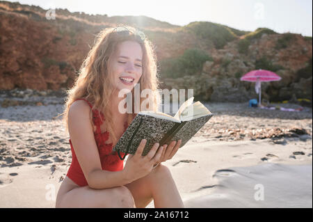 Glückliche junge Frau liest Buch am Strand Stockfoto