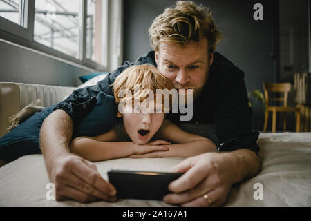 Portrait von Vater und Sohn auf der Couch liegend auf dem Mobiltelefon suchen Stockfoto