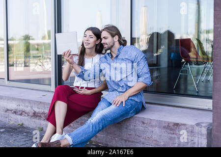 Junges Paar sitzt auf der Fensterbank bei Verwendung eines Tablet Gebäude Stockfoto