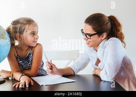 Lächelnd Lehrerin und Schülerin sitzen am Schreibtisch mit Kugel Stockfoto