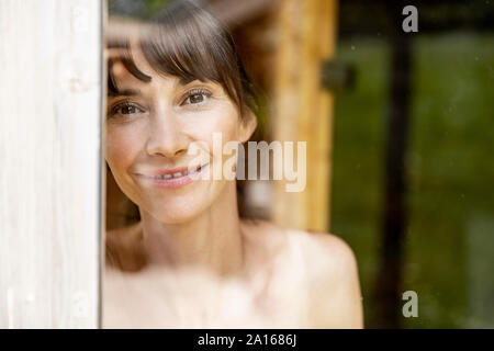 Portrait von lächelnden Frau hinter Fensterglas in der Sauna Stockfoto