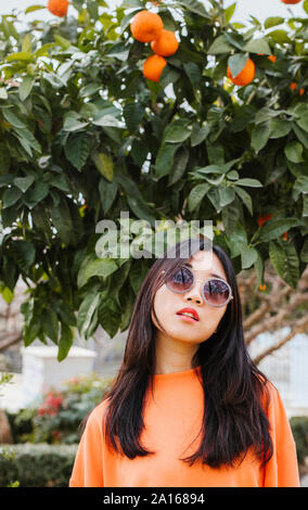 Portrait von jungen asiatischen Frau, Tangerine Baum im Hintergrund Stockfoto