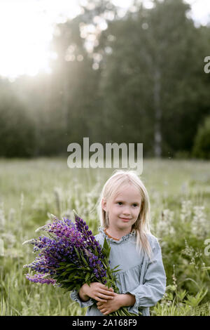 Portrait von blondes Mädchen mit Bündel von lupinen auf einer Wiese Stockfoto