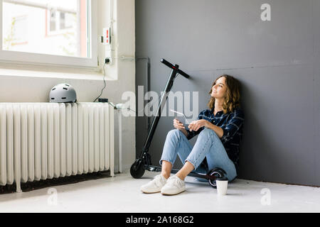 Junge Frau mit e-Scooter sitzen auf dem Boden, mit digitalen Tablet Stockfoto