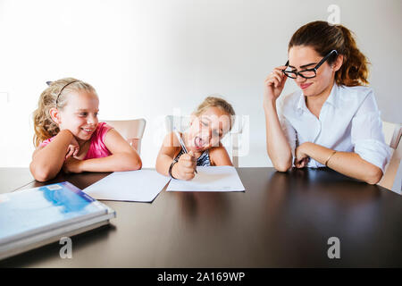 Lehrer am Schreibtisch sitzend mit zwei glückliche Schülerinnen Schreiben auf Papier Stockfoto