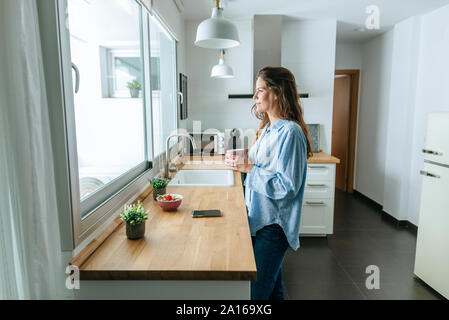 Junge Frau mit Pyjama in der Küche zu Hause Blick aus Fenster Stockfoto
