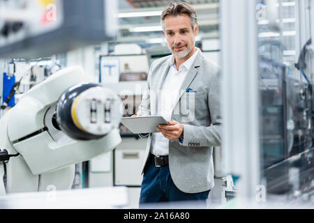 Geschäftsmann mit Tablette montageroboter in einer Fabrik Stockfoto