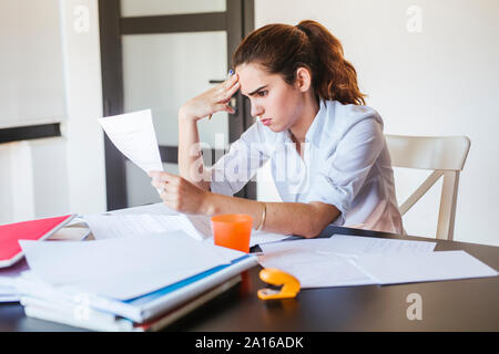 Studentin mit Dokumenten, die am Schreibtisch zu Hause Stockfoto