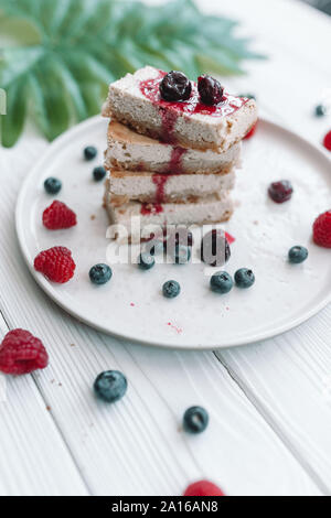 Scheiben von klassischen Käsekuchen mit frischen Beeren auf dem weißen Teller. Käsekuchen mit Heidelbeeren und Himbeeren. Stockfoto