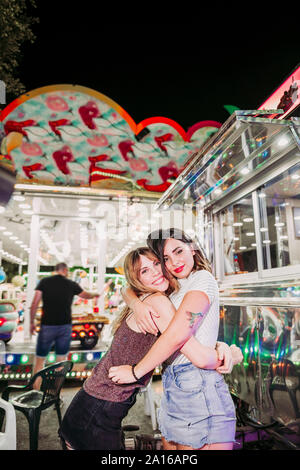 Porträt von zwei glückliche junge Frauen umarmen auf einem Jahrmarkt bei Nacht Stockfoto