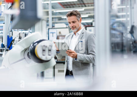 Geschäftsmann mit Tablette montageroboter in einer Fabrik Stockfoto