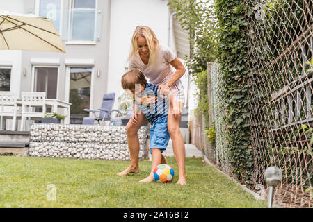 Glückliche Mutter und Sohn im Garten Fußball spielen Stockfoto