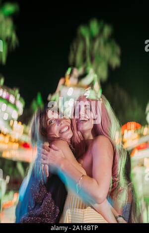 Porträt von zwei neugierige junge Frauen umarmen auf einem Jahrmarkt bei Nacht Stockfoto