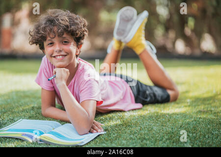 Portrait von lächelnden Jungen im Garten liegend Hausaufgaben Stockfoto