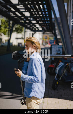 Junger Mann mit Handy für den e-Roller in der Stadt Stockfoto