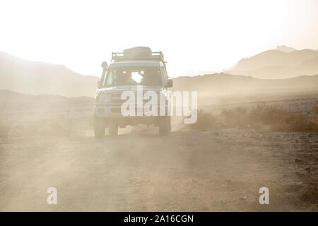 Off-road-Fahrzeug auf unbefestigte Straße inmitten von Staub in der Wüste gegen Himmel bei Sonnenuntergang Stockfoto