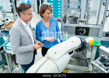 Geschäftsmann mit Tablet und Frau sprechen bei der Montage Roboter in einer Fabrik Stockfoto