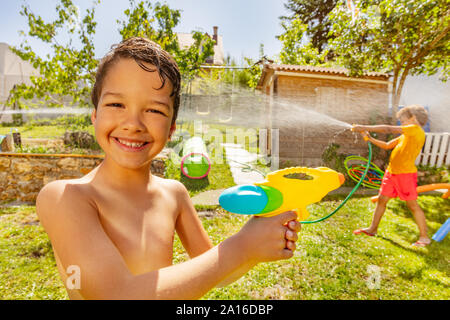 Sommer heissen Tag Spiel zwei Kinder mit Wasserpistole und Gartenschlauch Sprinkler glücklich Spielen Stockfoto