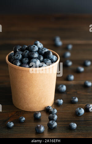 Frische organische Blaubeeren in einem Pappbecher. Dunkler Holztisch, hohe Auflösung Stockfoto