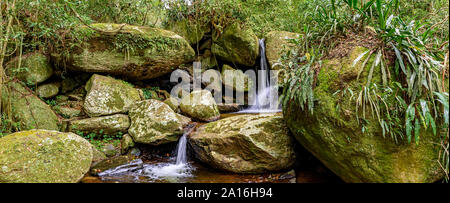 Kleiner Wasserfall Panoramablick zu den Regenwald Vegetation der Insel Ilhabela mit bemoosten Steinen an der Nordküste von Sao Paulo, Brasilien Stockfoto