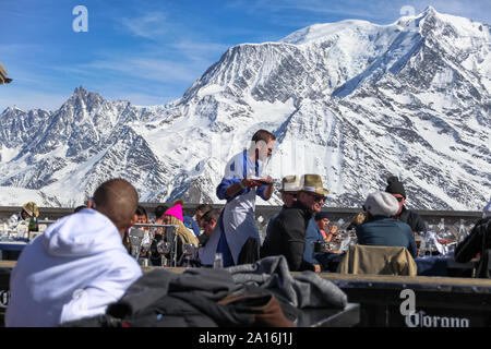 Weinkellner bedient Kunden mit Weindekanter. Der Mont-Blanc im Rücken an einem sonnigen Tag. La Folie Douce Saint Gervais Apres Skirestaurant von Chamonix. Stockfoto