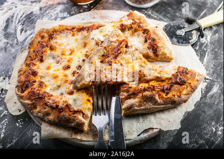 Quattro Formaggi Pizza Scheiben auf einem runden Schneidbrett auf einem dunklen Holztisch. Close-up Stockfoto