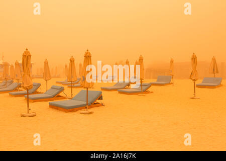 DUBAI - Leere Liegestühle und Sonnenschirme am Strand in Dubai Marina durch den Dunst der massiven Sandsturm, dass die Emirate am Donnerstag schlagen gesehen. Stockfoto