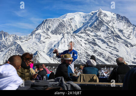 Weinkellner bedient Kunden mit Weindekanter. Der Mont-Blanc im Rücken an einem sonnigen Tag. La Folie Douce Saint Gervais Nach Ski Restaurantof Chamonix. Stockfoto