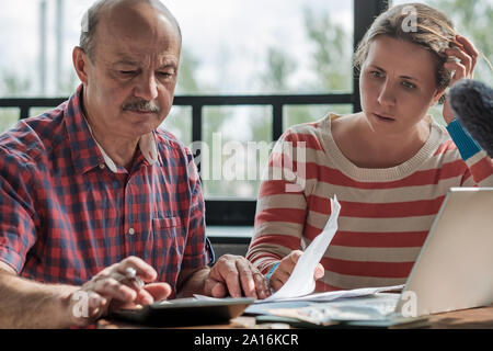 Olderly spanischer Mann zählen Geld mit seiner Tochter im Wohnzimmer sitzen. Hilfe für Kinder und Rentner. Stockfoto