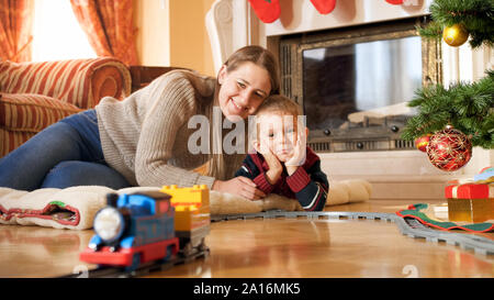 Portrait von Glücklich lächelnde Familie liegen auf dem Boden und auf der Bahn reiten auf die Bahn unter dem Weihnachtsbaum im Wohnzimmer Stockfoto