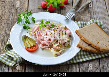 Herzhafte bayerische Wurstsalat mit Käse Streifen, Essiggurken und rustikales Bauernbrot Stockfoto