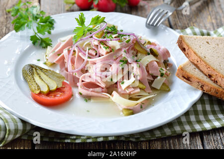 Herzhafte bayerische Wurstsalat mit Käse Streifen, Essiggurken und rustikales Bauernbrot Stockfoto