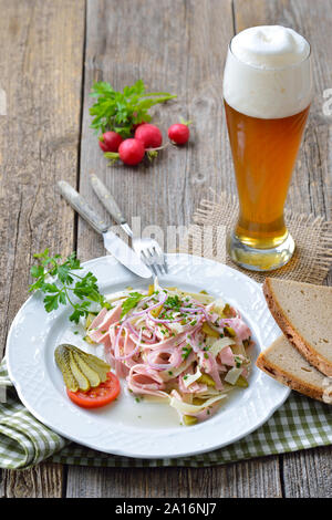 Herzhafte bayerische Wurstsalat mit Käse Streifen, Essiggurken und rustikales Bauernbrot serviert mit einem kühlen Weißbier Stockfoto